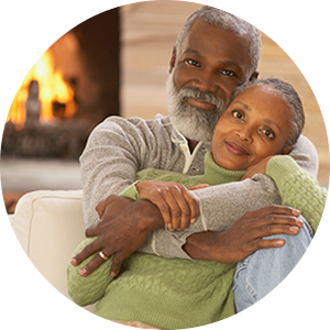 Couple hugging on their couch with a warm fireplace glowing in the background.