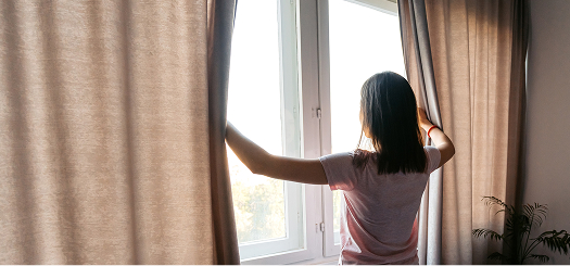 Woman opening curtains in her home and looking outside.